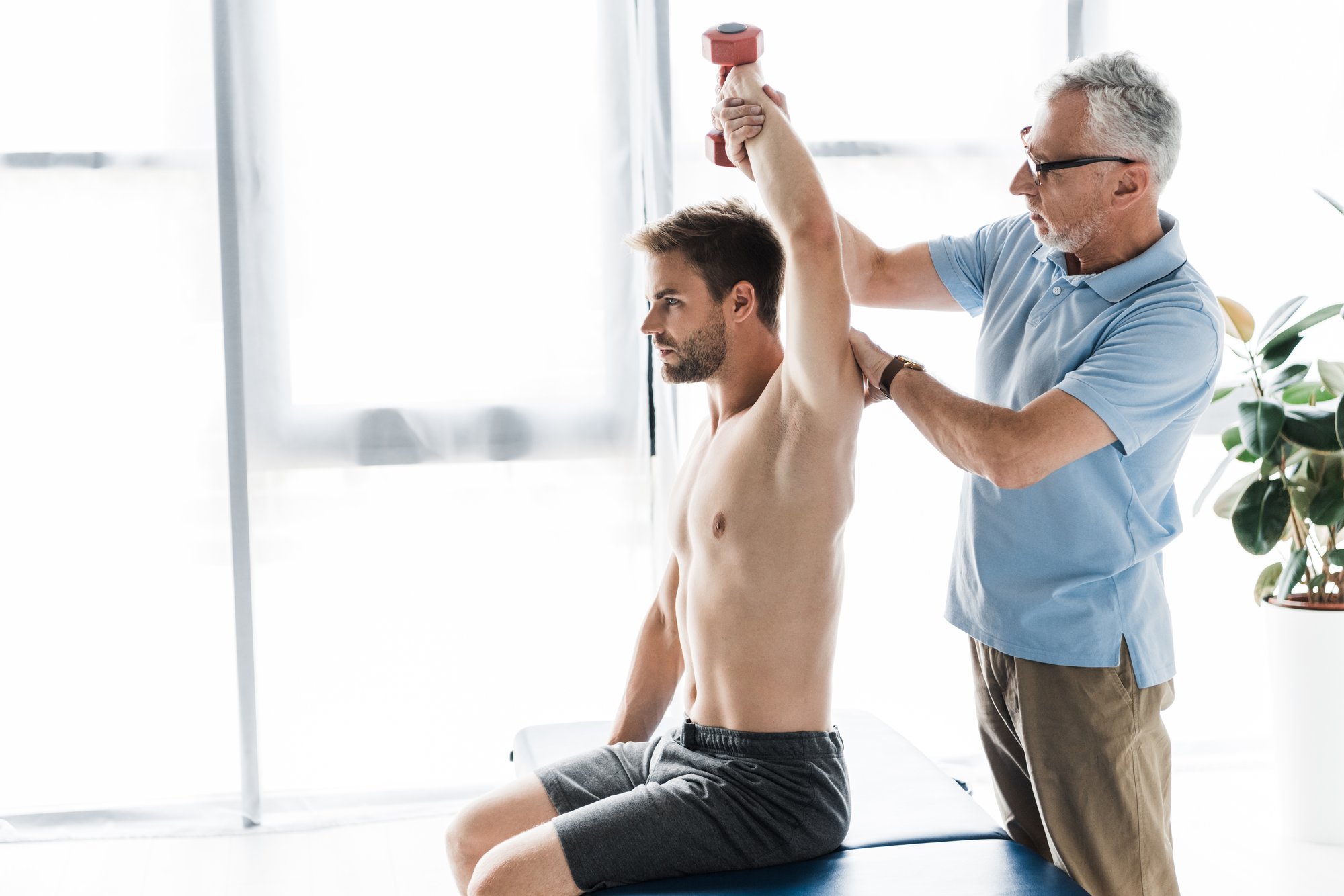 chiropractor-standing-near-man-exercising-with-dum-2024-11-13-07-11-34-utc